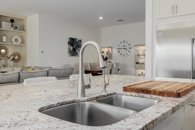 kitchen with white cabinetry, sink, light stone countertops, and stainless steel built in fridge