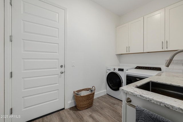 washroom featuring sink, washing machine and dryer, cabinets, and light wood-type flooring