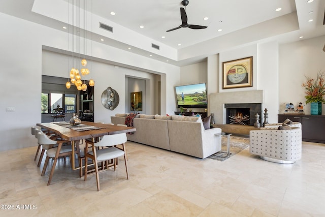 living room featuring a towering ceiling, a fireplace, a raised ceiling, and ceiling fan with notable chandelier