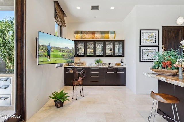 bar featuring light stone counters and dark brown cabinetry