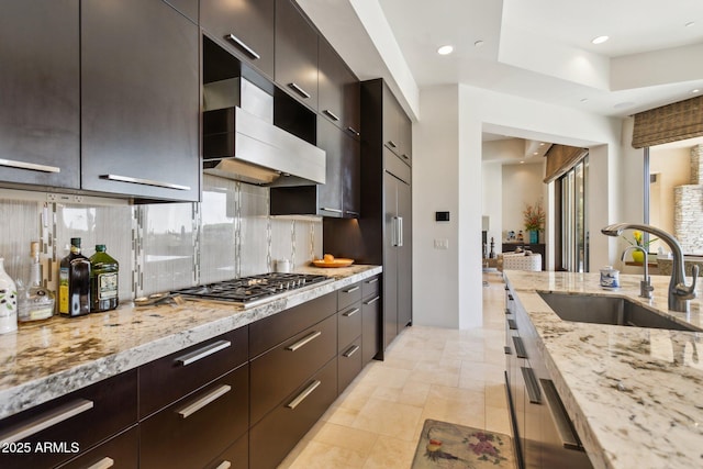 kitchen featuring range hood, stainless steel gas stovetop, sink, decorative backsplash, and light stone countertops