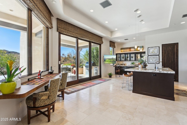 kitchen with pendant lighting, sink, a kitchen bar, a raised ceiling, and a center island with sink