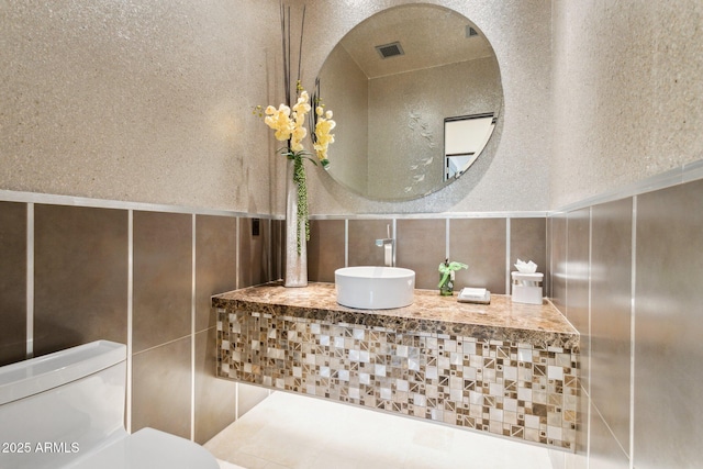 bathroom featuring toilet, sink, and tile walls