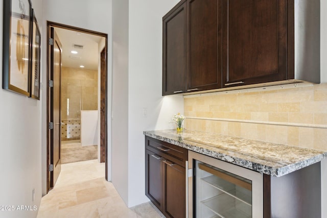 kitchen featuring dark brown cabinets, backsplash, beverage cooler, and light stone counters