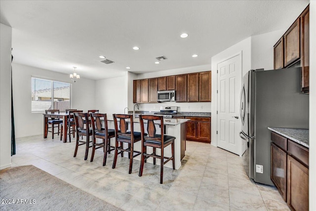 kitchen with sink, a kitchen breakfast bar, stainless steel appliances, an inviting chandelier, and a kitchen island with sink