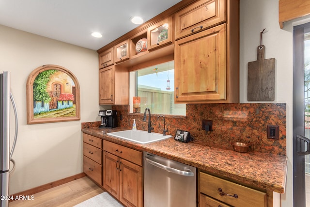 kitchen with stainless steel appliances, sink, tasteful backsplash, dark stone counters, and light wood-type flooring