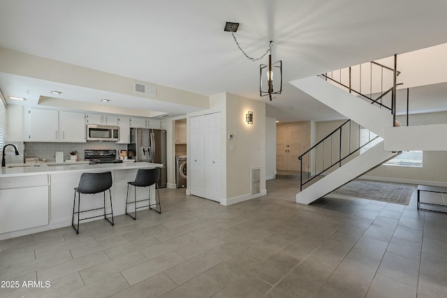 kitchen featuring visible vents, a peninsula, washer / clothes dryer, a sink, and appliances with stainless steel finishes