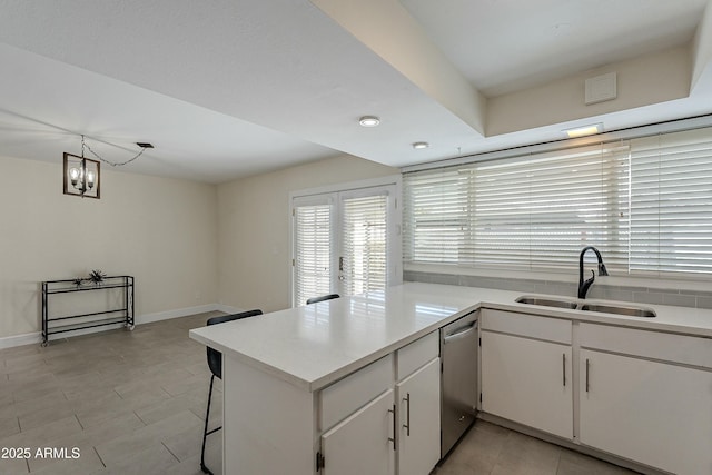 kitchen with a sink, light countertops, a peninsula, white cabinets, and stainless steel dishwasher