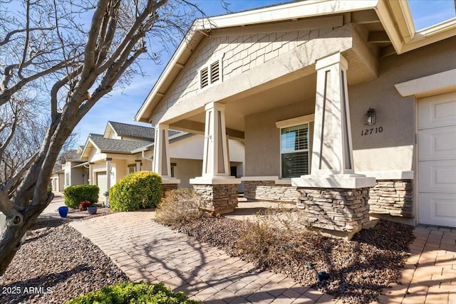 view of side of home featuring a garage, stone siding, covered porch, and stucco siding