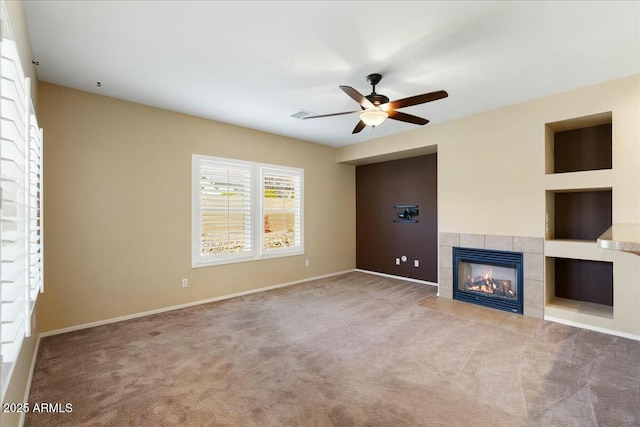 unfurnished living room with carpet floors, a tile fireplace, a ceiling fan, and baseboards