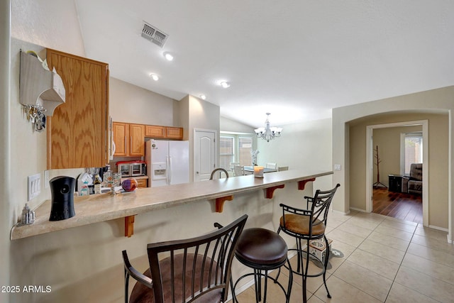 9926 W Gross Ave, Tolleson, AZ 85353 - kitchen featuring white refrigerator with ice dispenser, lofted ceiling, a peninsula, light countertops, and a kitchen bar