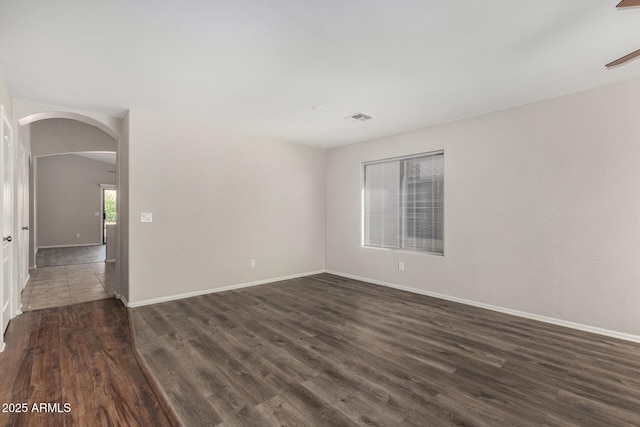 unfurnished room with baseboards, visible vents, arched walkways, and dark wood-style floors
