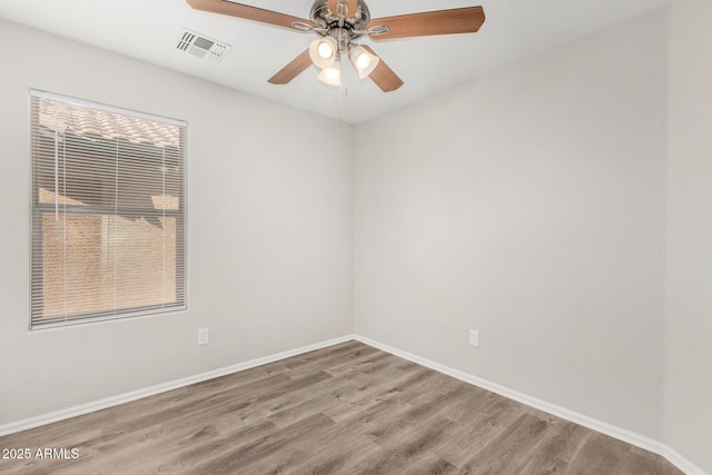 empty room with wood finished floors, visible vents, a ceiling fan, and baseboards