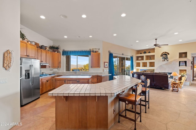 kitchen with ceiling fan, sink, tile countertops, stainless steel fridge with ice dispenser, and a breakfast bar area