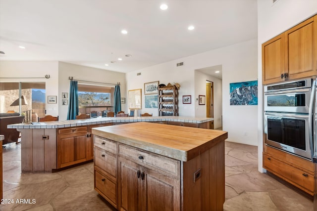 kitchen featuring wood counters, a center island, stainless steel double oven, and kitchen peninsula