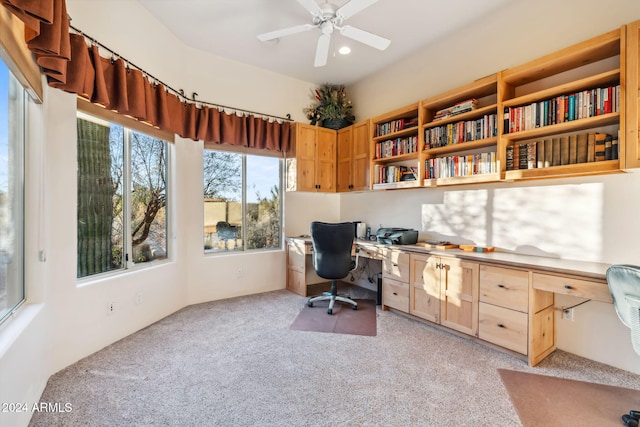 home office featuring ceiling fan, built in desk, and light carpet