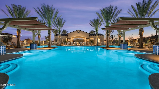 pool at dusk with a patio area and a pergola