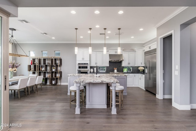 kitchen with white cabinets, hanging light fixtures, an island with sink, and stainless steel appliances