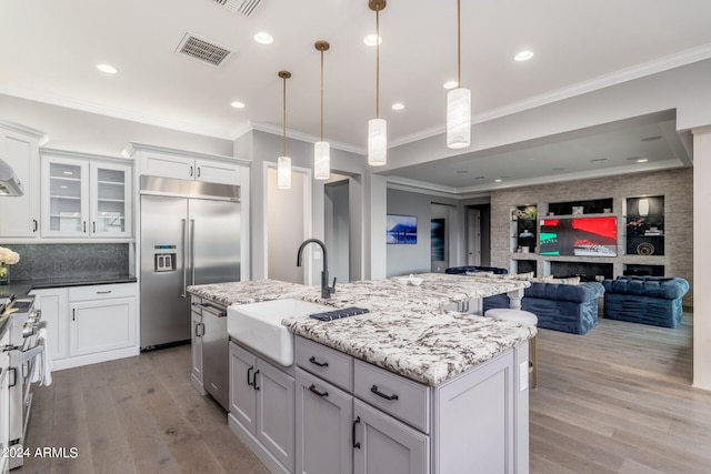 kitchen featuring pendant lighting, appliances with stainless steel finishes, a kitchen island with sink, and light hardwood / wood-style flooring