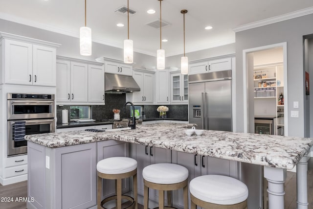 kitchen with extractor fan, appliances with stainless steel finishes, a large island with sink, and hanging light fixtures