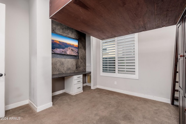 unfurnished office featuring built in desk, light colored carpet, and wood ceiling