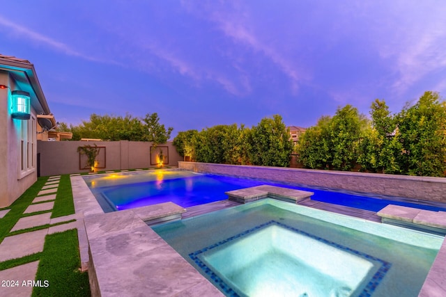 pool at dusk featuring an in ground hot tub