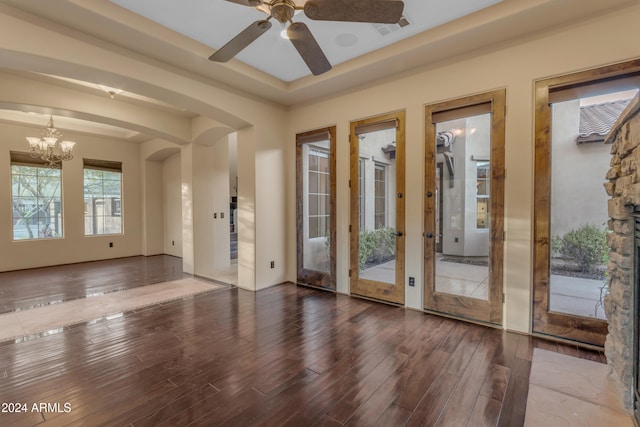 entryway with ceiling fan with notable chandelier, a raised ceiling, and dark wood-type flooring