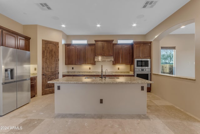 kitchen with light stone countertops, sink, stainless steel appliances, and an island with sink