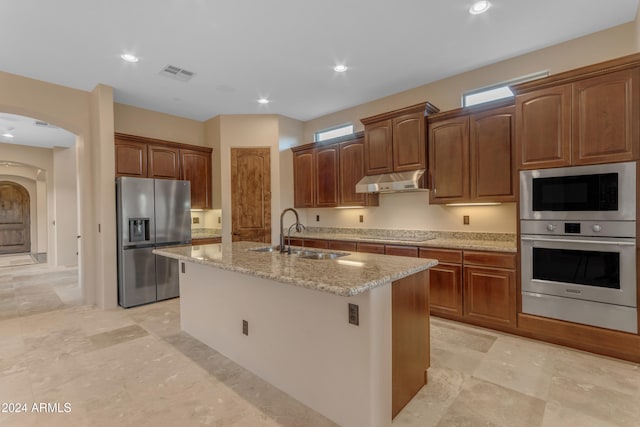 kitchen featuring stainless steel appliances, light stone counters, a kitchen island with sink, and sink