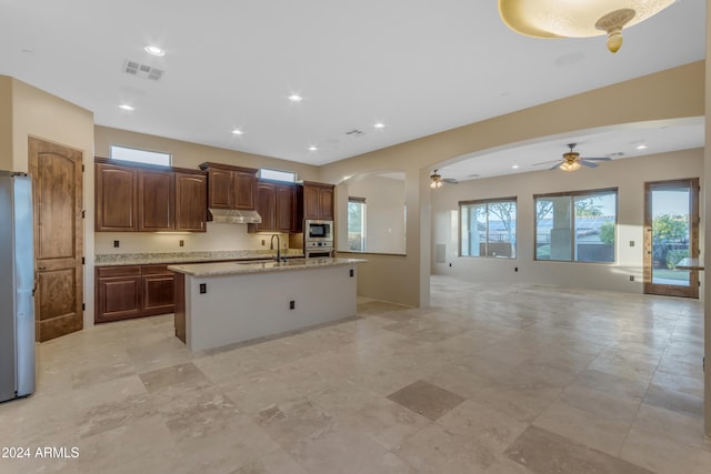 kitchen featuring appliances with stainless steel finishes, light stone counters, ceiling fan, sink, and an island with sink