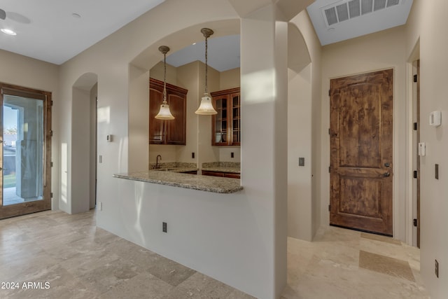 kitchen featuring pendant lighting, kitchen peninsula, light stone countertops, and sink