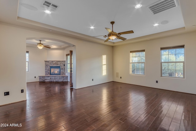 unfurnished living room with a fireplace, a tray ceiling, dark hardwood / wood-style floors, and ceiling fan