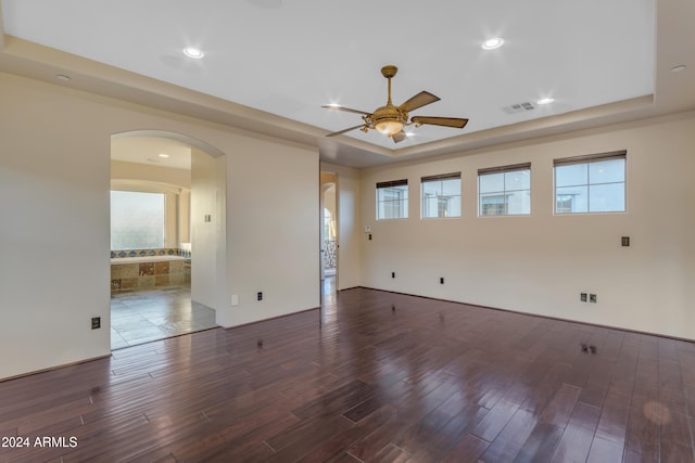 unfurnished room featuring a tray ceiling, ceiling fan, and dark hardwood / wood-style floors