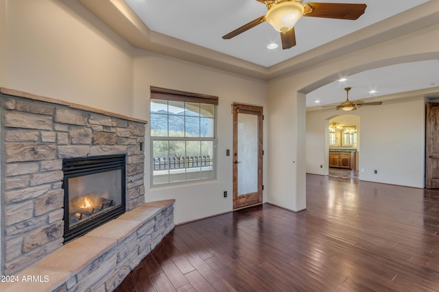 unfurnished living room featuring dark hardwood / wood-style floors, a stone fireplace, and ceiling fan