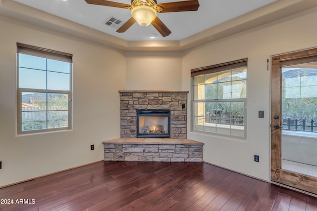 unfurnished living room with dark hardwood / wood-style flooring, a stone fireplace, and ceiling fan