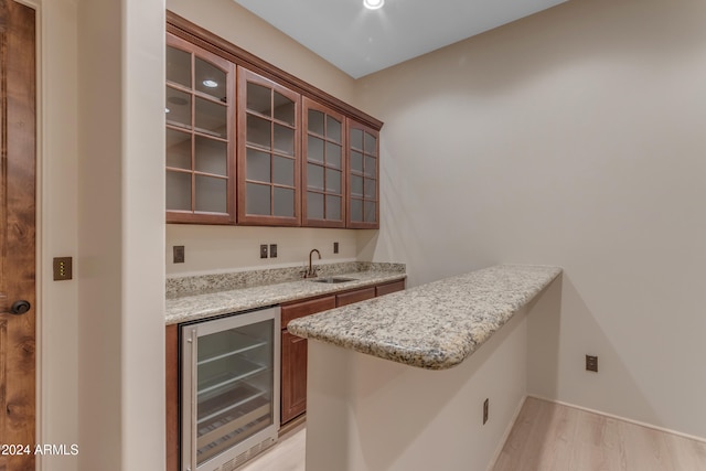 bar with light stone counters, sink, beverage cooler, and light hardwood / wood-style flooring