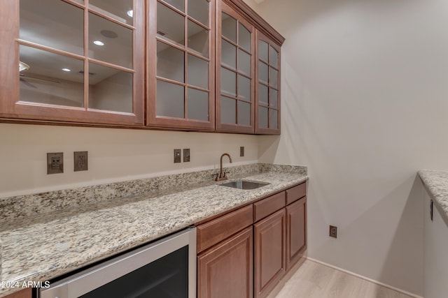 bar with light hardwood / wood-style floors, light stone counters, sink, and wine cooler