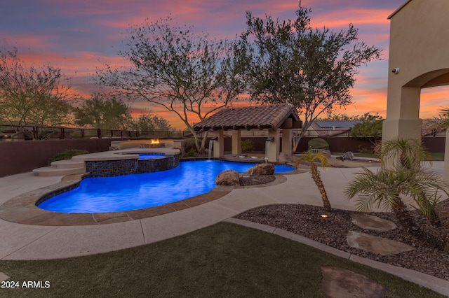 pool at dusk with an in ground hot tub and a patio area