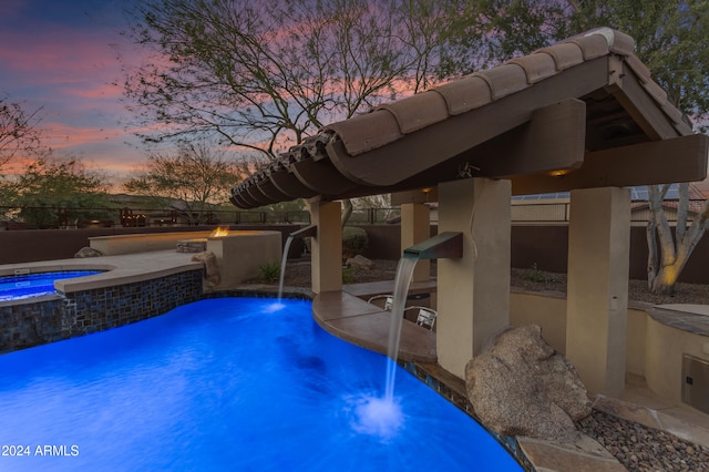 pool at dusk with an in ground hot tub, pool water feature, a patio, and a fire pit