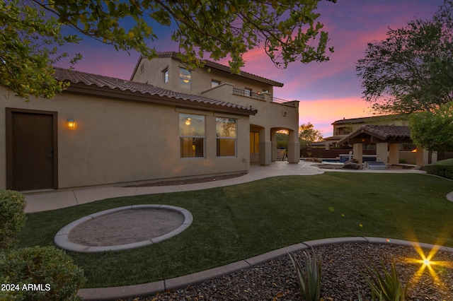 back house at dusk with a lawn, a balcony, and a patio