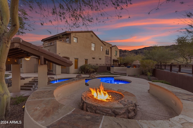 pool at dusk featuring pool water feature, an in ground hot tub, and an outdoor fire pit