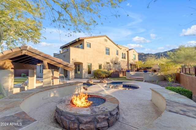 back of property featuring a mountain view, a patio, an outdoor fire pit, and an outdoor hot tub