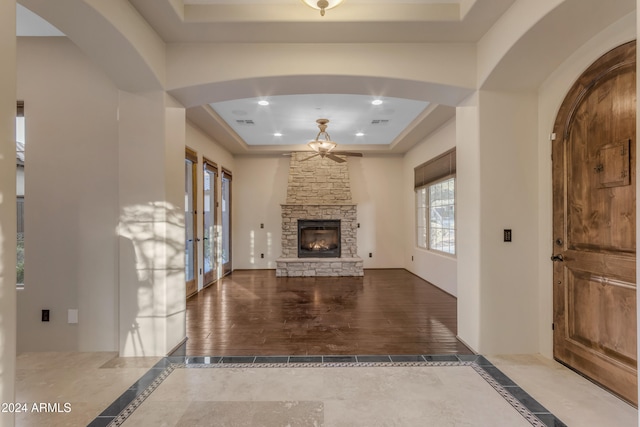 unfurnished living room featuring a fireplace, french doors, a tray ceiling, and ceiling fan