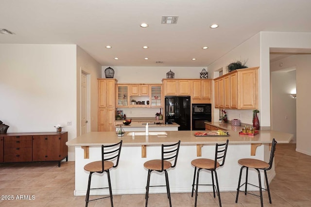 kitchen with black appliances, light tile patterned floors, light brown cabinetry, kitchen peninsula, and a breakfast bar area