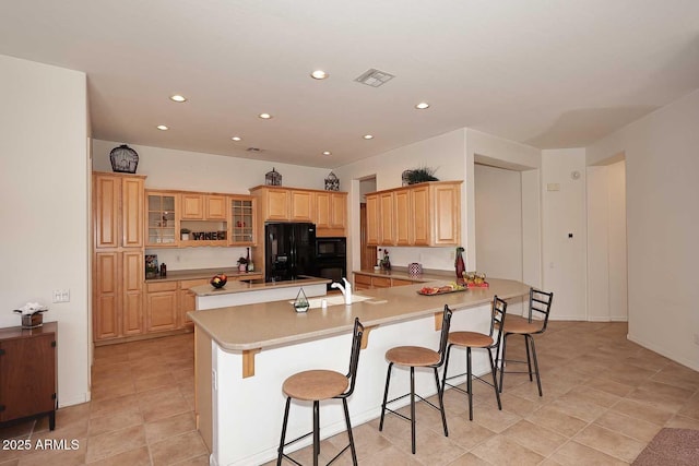 kitchen featuring kitchen peninsula, a kitchen breakfast bar, light brown cabinetry, and black appliances