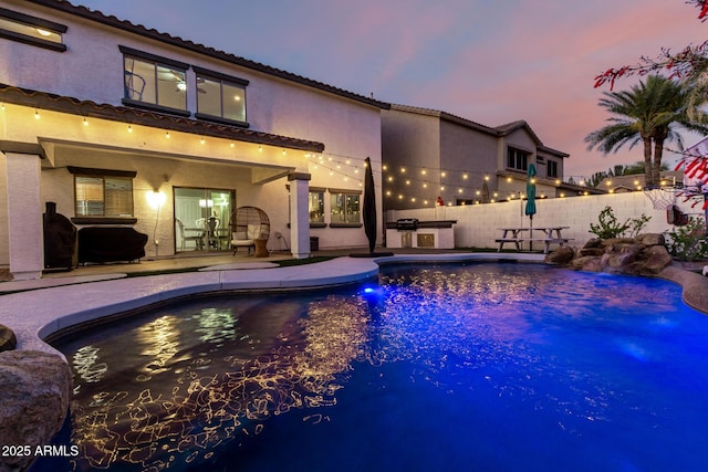 1429 E Lowell Ave, Gilbert, AZ 85295 - pool at dusk featuring an outdoor kitchen, a patio area, and fence