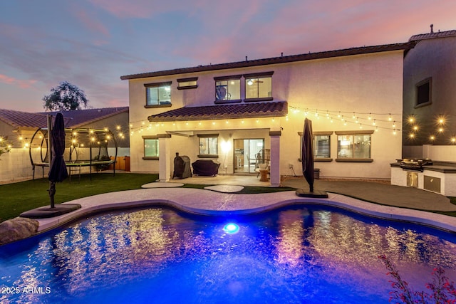 1429 E Lowell Ave, Gilbert, AZ 85295 - back of property at dusk with exterior kitchen, a trampoline, a patio area, and a fenced backyard