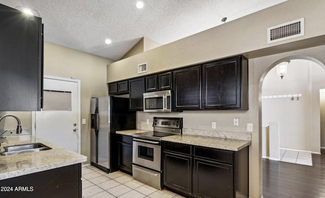 kitchen featuring a textured ceiling, sink, appliances with stainless steel finishes, and vaulted ceiling