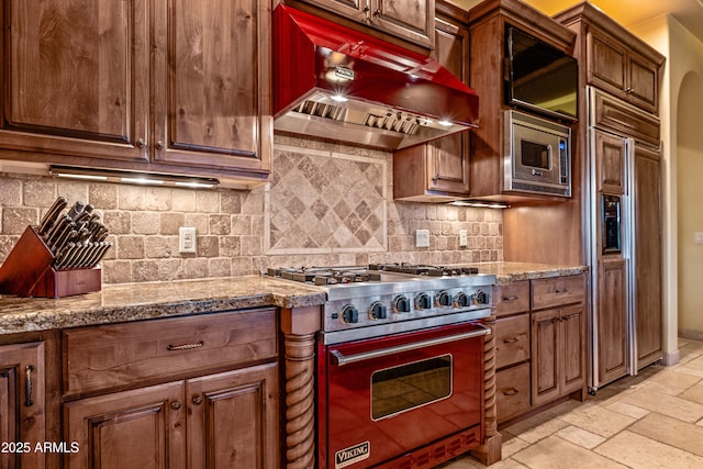 kitchen with built in appliances, decorative backsplash, light stone countertops, and custom range hood