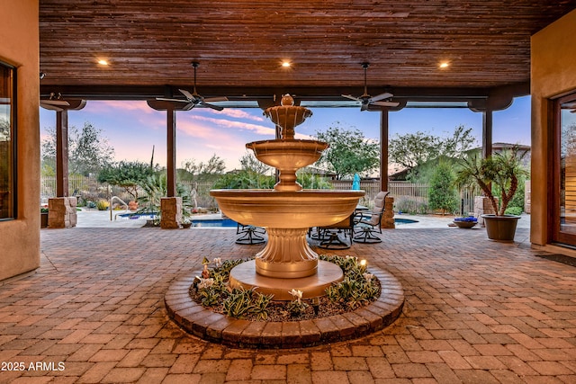 patio terrace at dusk with a fenced in pool and ceiling fan